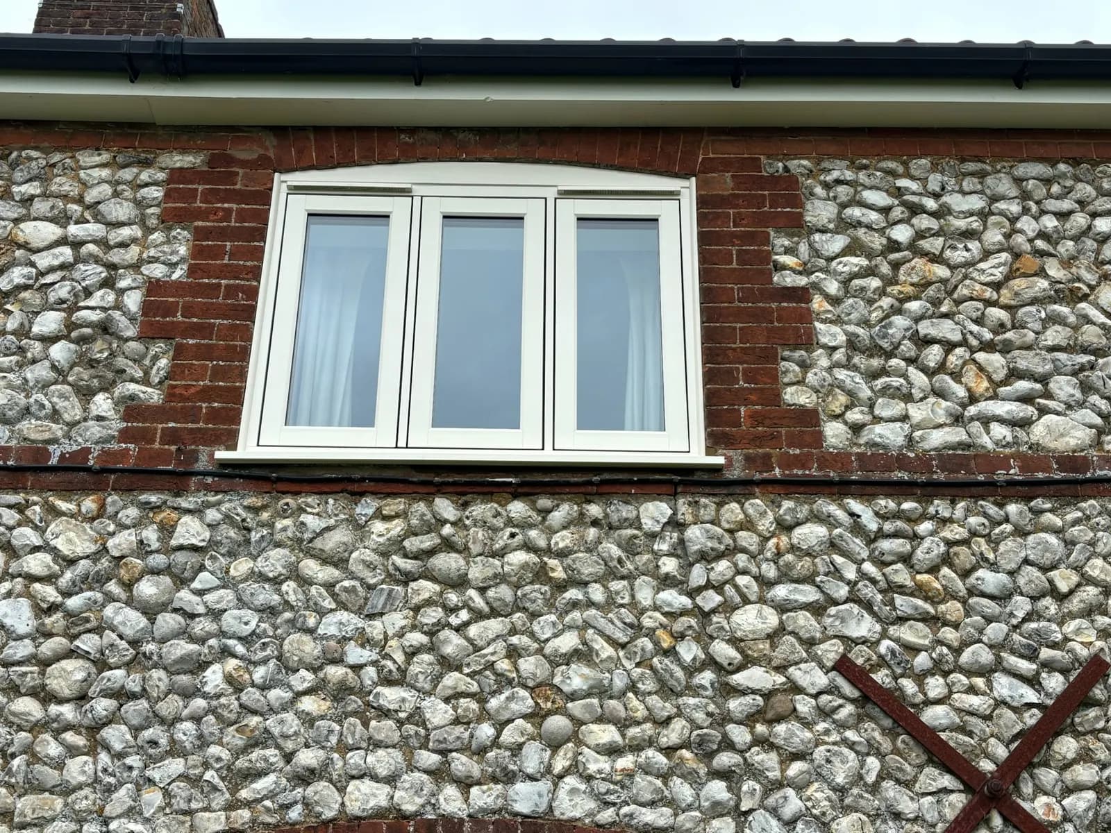 Light-coloured cottage window in a brick-and-flint wall